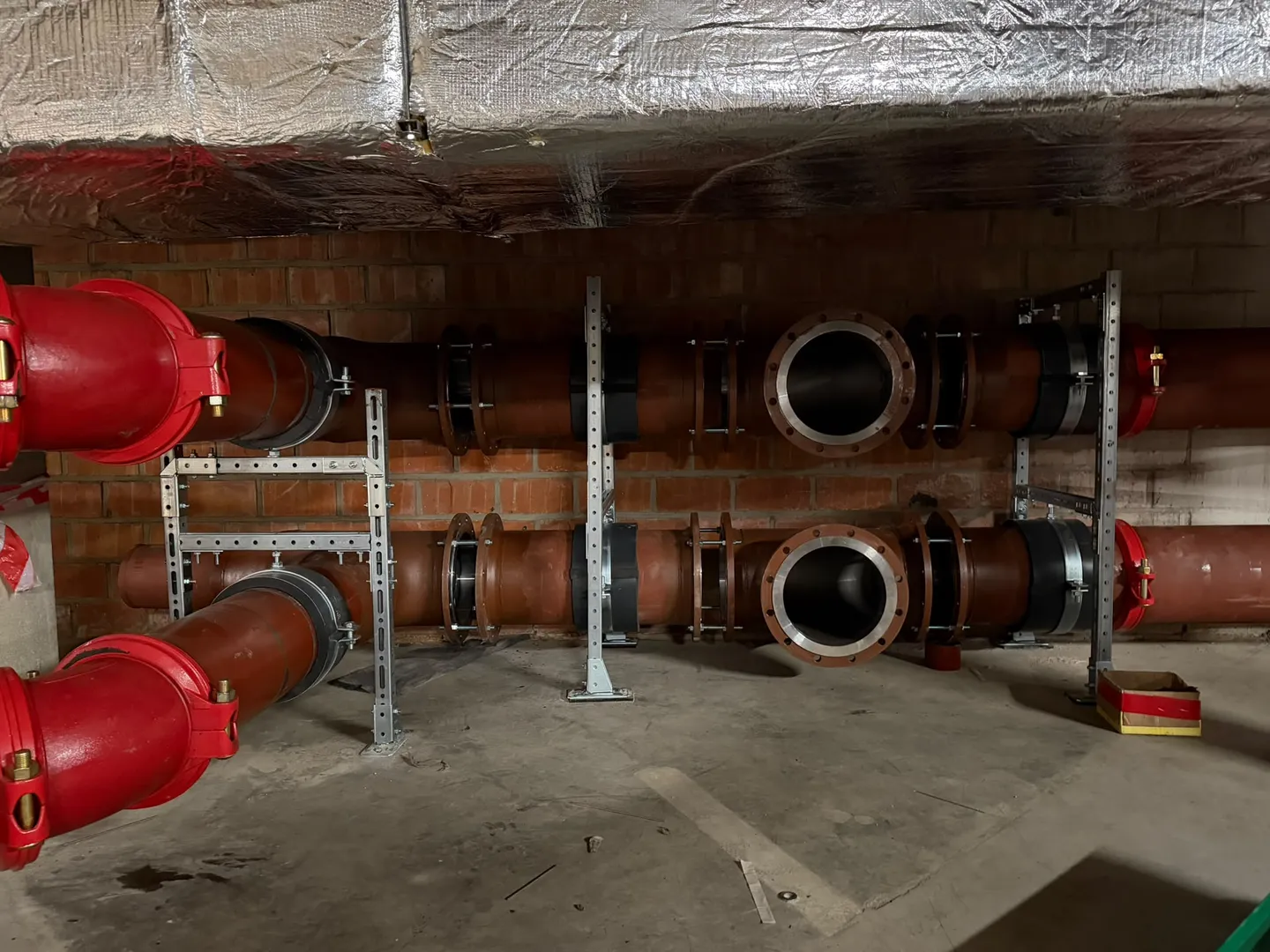 Large-diameter flanged pipework with grooved couplings mounted on steel supports in a basement